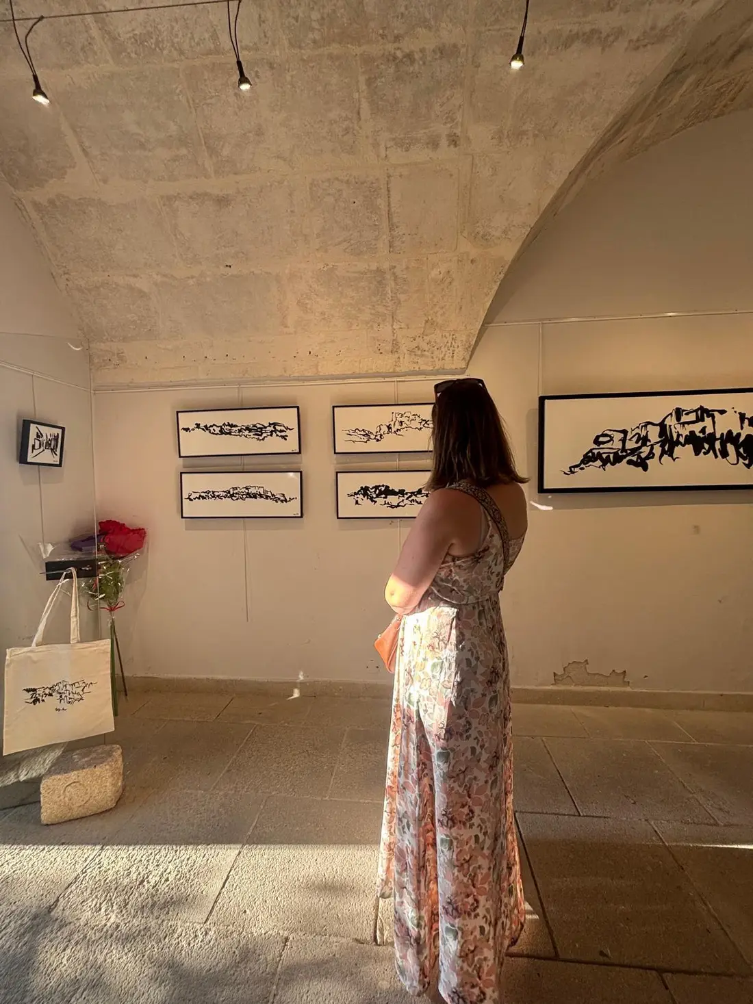 Vue de l'exposition à la Galerie La Cure : dessins encadrés des Baux-de-Provence accrochés sous la voûte de pierre.